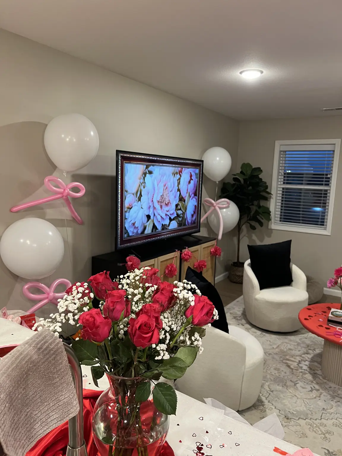 Living room styled with white balloons, pink balloon bows, and red roses